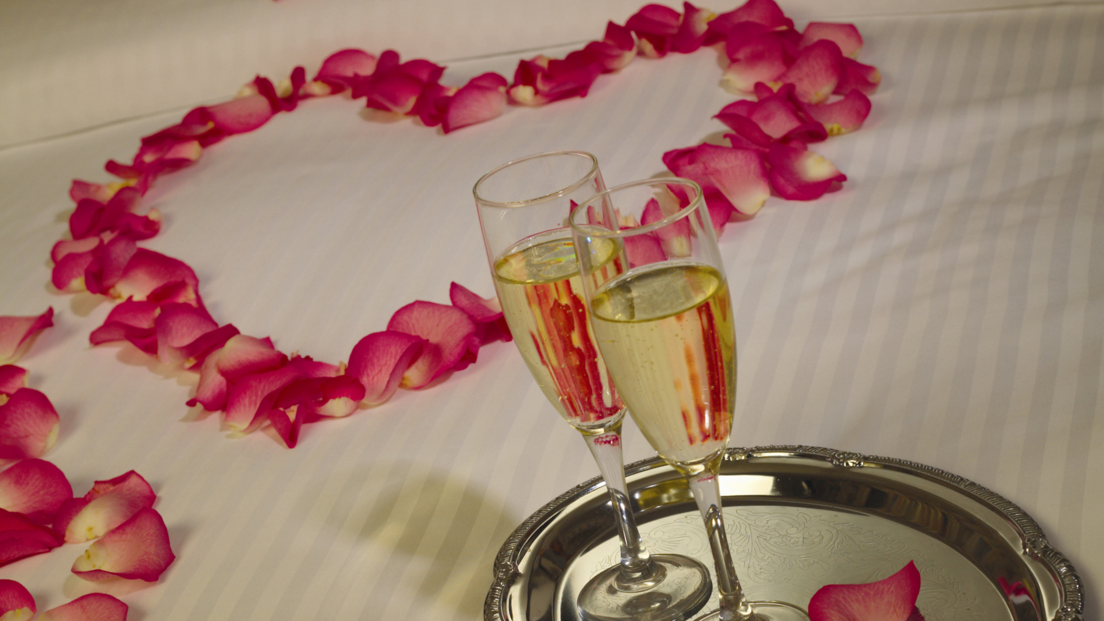 Rose-petals-in-a-heart-on-bed-with-champagne